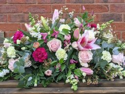 A tapered and structured display of diffierent toned pink and cream funeral flowers.